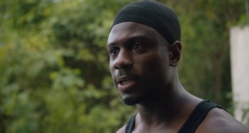 Movie still from “The Day Shall Come” (2019), directed by Christopher Morris – A person wearing a black hat; Close Up shot, Over the shoulder angle