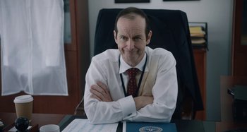 Movie still from “The Day Shall Come” (2019), directed by Christopher Morris – A man sitting at a desk with his arms crossed; Close Up shot, Over the shoulder angle