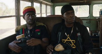 Movie still from “The Day Shall Come” (2019), directed by Christopher Morris – A couple of men sitting next to each other on top of a bus; Medium shot, Over the shoulder angle