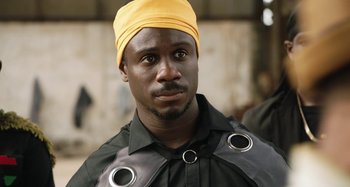 Movie still from “The Day Shall Come” (2019), directed by Christopher Morris – A man wearing a yellow hat and a black shirt; Close Up shot, Over the shoulder angle