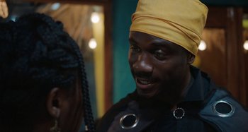 Movie still from “The Day Shall Come” (2019), directed by Christopher Morris – A man wearing a yellow hat and a black shirt; Close Up shot, Over the shoulder angle