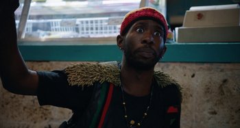 Movie still from “The Day Shall Come” (2019), directed by Christopher Morris – A man wearing a red hat and a black jacket; Close Up shot, Low angle