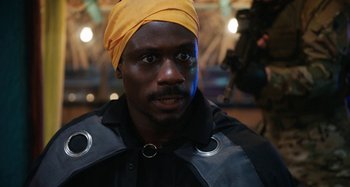 Movie still from “The Day Shall Come” (2019), directed by Christopher Morris – A man wearing a yellow head scarf and a black jacket; Close Up shot, Over the shoulder angle