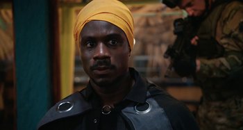 Movie still from “The Day Shall Come” (2019), directed by Christopher Morris – A man with a yellow turban on his head; Close Up shot, Over the shoulder angle