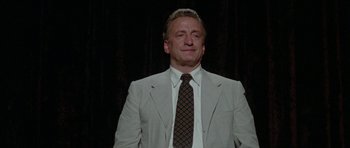 Movie still from “The Day of the Dolphin” (1973), directed by Mike Nichols – A man wearing a suit and tie standing in front of a black background; Medium shot, Low angle