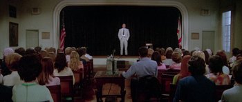 Movie still from “The Day of the Dolphin” (1973), directed by Mike Nichols – A man standing on a stage in front of a group of people; Wide shot, High angle