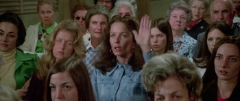 Movie still from “The Day of the Dolphin” (1973), directed by Mike Nichols – A group of people in a room with one woman raising her hand; Medium shot, High angle