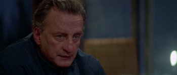 Movie still from “The Day of the Dolphin” (1973), directed by Mike Nichols – A person sitting at a table; Close Up shot, Over the shoulder angle