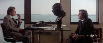 Movie still from “The Day of the Dolphin” (1973), directed by Mike Nichols – A statue of a man sitting at a desk; Medium shot, Over the shoulder angle