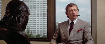 Movie still from “The Day of the Dolphin” (1973), directed by Mike Nichols – A man sitting in front of a window in a suit and tie; Medium shot, Over the shoulder angle