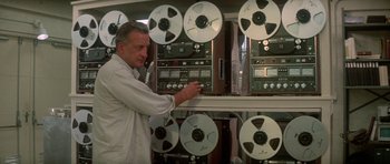 Movie still from “The Day of the Dolphin” (1973), directed by Mike Nichols – An older man in a white lab coat is looking at some tapes; Close Up shot, High angle