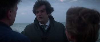 Movie still from “The Day of the Dolphin” (1973), directed by Mike Nichols – A man in a jacket and tie talking to another man in front of a body of water; Close Up shot, Over the shoulder angle