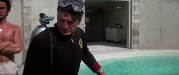 Movie still from “The Day of the Dolphin” (1973), directed by Mike Nichols – An older man in a wetsuit in a swimming pool; Medium shot, Over the shoulder angle