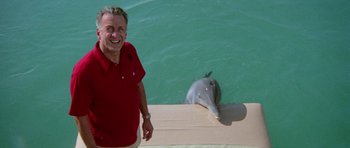 Movie still from “The Day of the Dolphin” (1973), directed by Mike Nichols – A man standing next to a dolphin in the water; Medium shot, Low angle