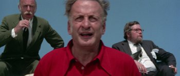 Movie still from “The Day of the Dolphin” (1973), directed by Mike Nichols – An older man in a red shirt is looking at the camera; Close Up shot, Low angle
