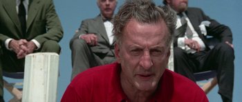 Movie still from “The Day of the Dolphin” (1973), directed by Mike Nichols – An older man in a red shirt is looking at the camera; Close Up shot, Low angle