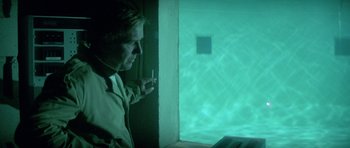 Movie still from “The Day of the Dolphin” (1973), directed by Mike Nichols – A man smoking a cigarette in front of an open window; Medium shot, Over the shoulder angle