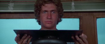 Movie still from “The Day of the Dolphin” (1973), directed by Mike Nichols – A man with curly hair holding a frying pan in front of his face; Close Up shot, Low angle