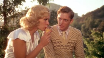 Movie still from “The Day of the Locust” (1975), directed by John Schlesinger – A man and a woman are eating a donut together; Medium shot, High angle