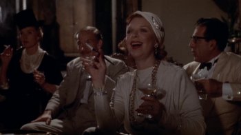 Movie still from “The Day of the Locust” (1975), directed by John Schlesinger – An older woman holding a glass of wine and a cigarette in her mouth; Medium shot, Low angle