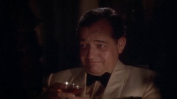 Movie still from “The Day of the Locust” (1975), directed by John Schlesinger – A person sitting at a table holding a drink; Close Up shot, High angle