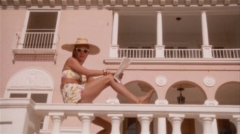 Movie still from “The Day of the Locust” (1975), directed by John Schlesinger – A woman sitting on a balcony reading a newspaper; Wide shot, Low angle
