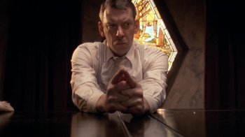 Movie still from “The Day of the Locust” (1975), directed by John Schlesinger – A man sitting at a table with his hands crossed; Close Up shot, Low angle