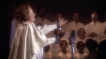 Movie still from “The Day of the Locust” (1975), directed by John Schlesinger – A woman in a white cape singing into a microphone; Medium shot, Over the shoulder angle