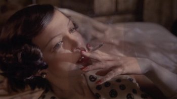 Movie still from “The Day of the Locust” (1975), directed by John Schlesinger – A woman smoking a cigarette while sitting on a couch; Close Up shot, Overhead angle