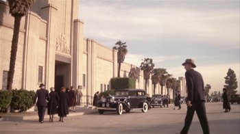 Movie still from “The Day of the Locust” (1975), directed by John Schlesinger – A group of people walking down a street past a building; Extreme Wide shot, Low angle