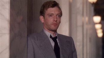 Movie still from “The Day of the Locust” (1975), directed by John Schlesinger – A man wearing a suit and tie standing in front of a wall; Close Up shot, Low angle