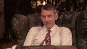 Movie still from “The Day of the Locust” (1975), directed by John Schlesinger – A man sitting in a chair wearing a white shirt and tie; Close Up shot, Low angle