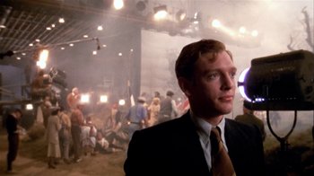 Movie still from “The Day of the Locust” (1975), directed by John Schlesinger – A man wearing a suit and tie standing in front of a group of people; Close Up shot, Over the shoulder angle