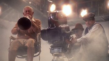 Movie still from “The Day of the Locust” (1975), directed by John Schlesinger – A group of people that are sitting around a camera; Wide shot, Low angle