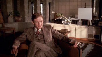 Movie still from “The Day of the Locust” (1975), directed by John Schlesinger – A man sitting on a couch holding a remote control; Medium shot, Low angle