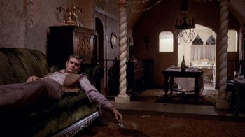 Movie still from “The Day of the Locust” (1975), directed by John Schlesinger – A man sitting on top of a couch in a living room; Wide shot, High angle