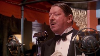 Movie still from “The Day of the Locust” (1975), directed by John Schlesinger – An older man in a black tuxedo is speaking into a microphone at an event; Close Up shot, Low angle