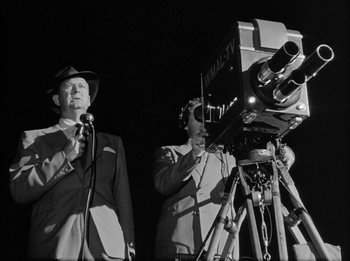 Movie still from “The Day the Earth Stood Still” (1951), directed by Robert Wise – Two men in suits and hats are standing in front of a video camera; Medium shot, Low angle