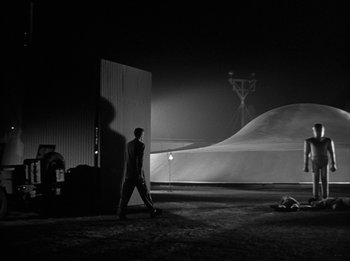 Movie still from “The Day the Earth Stood Still” (1951), directed by Robert Wise – A man is walking in the dark near a pile of sand; Extreme Wide shot, Over the shoulder angle