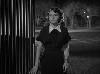 Movie still from “The Day the Earth Stood Still” (1951), directed by Robert Wise – A woman in a black dress standing next to a metal fence; Medium shot, Low angle