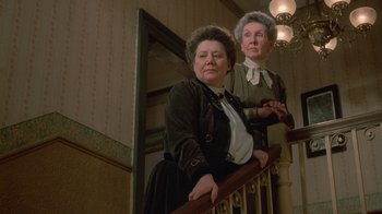 Movie still from “The Dead” (1987), directed by John Huston – Two older women standing at the top of a stair railing; Medium shot, Low angle