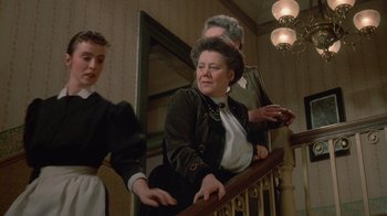 Movie still from “The Dead” (1987), directed by John Huston – An older woman sitting on top of a wooden railing; Medium shot, Low angle