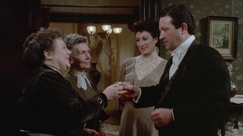 Movie still from “The Dead” (1987), directed by John Huston – A group of people standing next to each other holding drinks; Medium shot, High angle