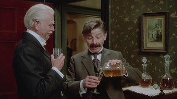 Movie still from “The Dead” (1987), directed by John Huston – A man pouring a drink into a wine glass while another man looks on; Medium shot, Low angle