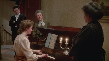 Movie still from “The Dead” (1987), directed by John Huston – A woman sitting at a piano in front of two men; Medium shot, High angle