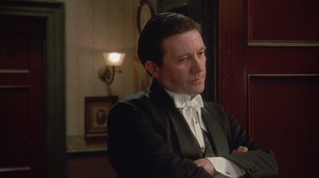 Movie still from “The Dead” (1987), directed by John Huston – A man in a suit and bow - tie is sitting down; Close Up shot, Low angle