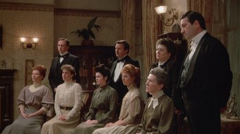 Movie still from “The Dead” (1987), directed by John Huston – A group of men and women sitting next to each other; Wide shot, High angle