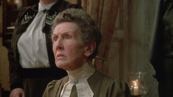 Movie still from “The Dead” (1987), directed by John Huston – An older woman wearing a dress and a tie; Close Up shot, Low angle