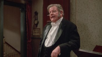 Movie still from “The Dead” (1987), directed by John Huston – An older man in a tuxedo standing in front of a wall; Medium shot, High angle