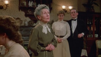 Movie still from “The Dead” (1987), directed by John Huston – An older woman standing in front of a group of people; Medium shot, Low angle